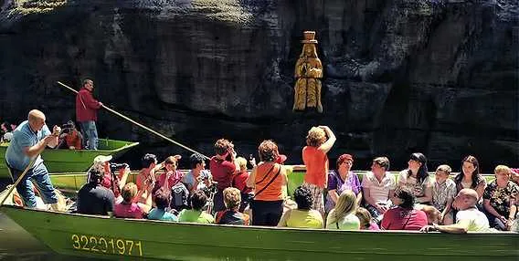 Turisté v lodi u sochy Panny Marie na řece.
