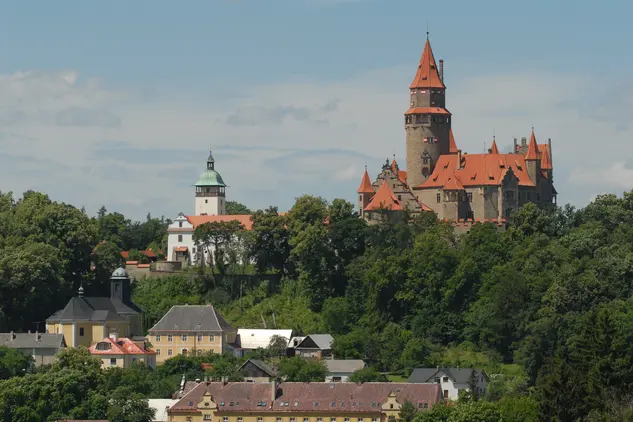 Zámek Bouzov na kopci nad městem s okolními domy.
