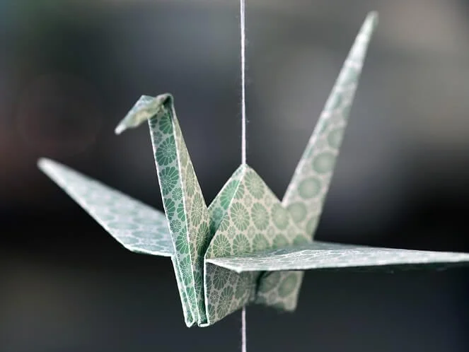 Zelený papírový pták skládaný technikou origami visící na provázku.