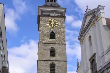 Historická věž s hodinami v Českých Budějovicích pod modrou oblohou.