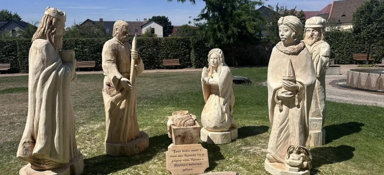 Skupina dřevěných soch biblických postav venku v parku.