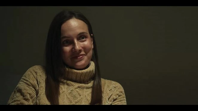 Žena v béžovém svetrku se úsměvem na tváři.
