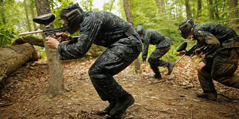 Tři hráči v kamufláži hrají paintball mezi stromy.