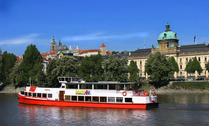 Turistická loď pluje po řece s historickým městem na pozadí.