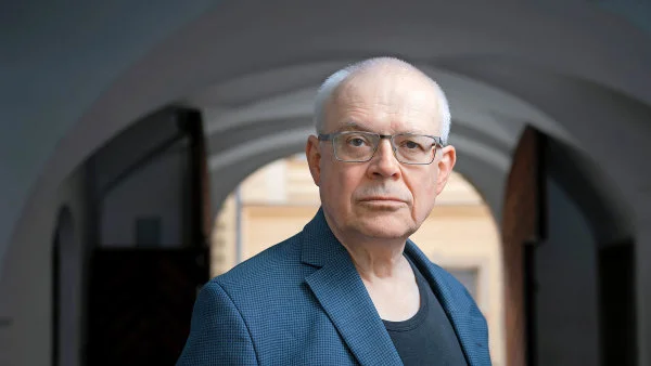 Portrét staršího muže v modrém kabátu pod oblouky.