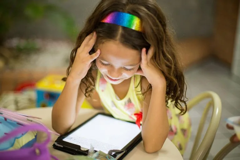 Dívka s barevnou čepicí používá tablet u stolu.
