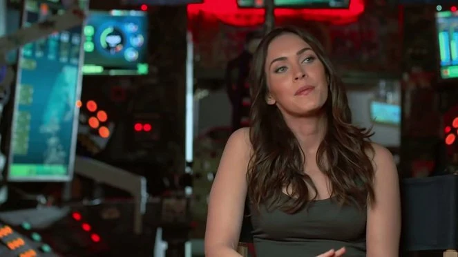 Herečka Megan Fox v záběru s počítačovými monitory na pozadí.