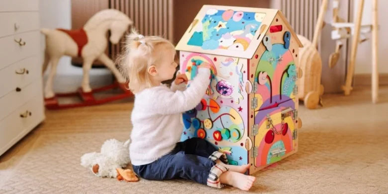 Malá dívka hraje s barevnou dřevěnou aktivní deskou ve tvaru domečku.