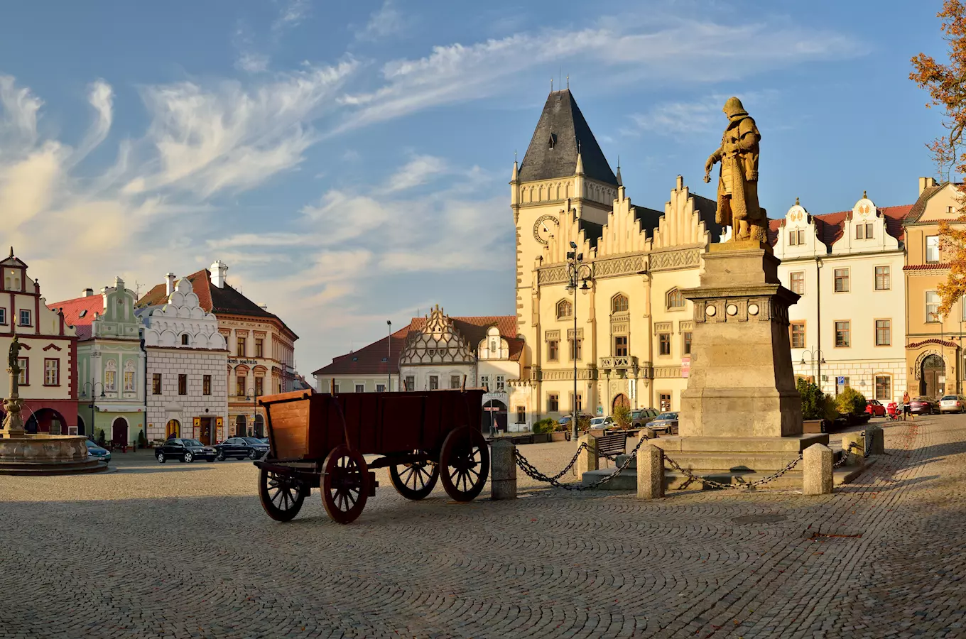 Náměstí v Tábore s sochou, starým vozem a historickými domy.