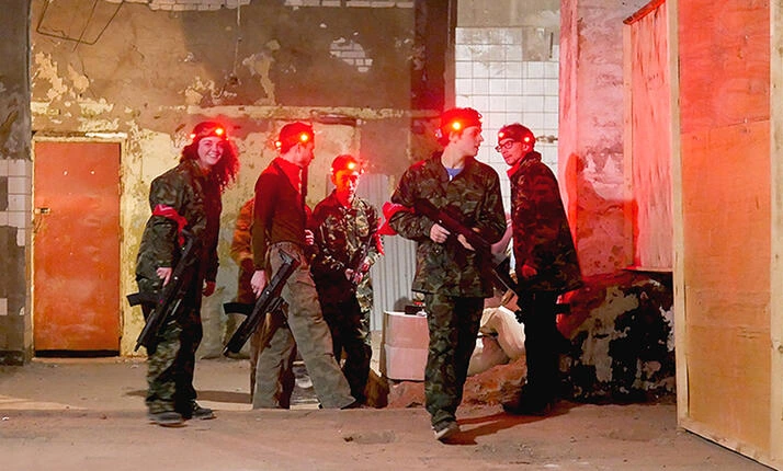 Skupina lidí v maskách a s lasery hraje ve venkovní hře.