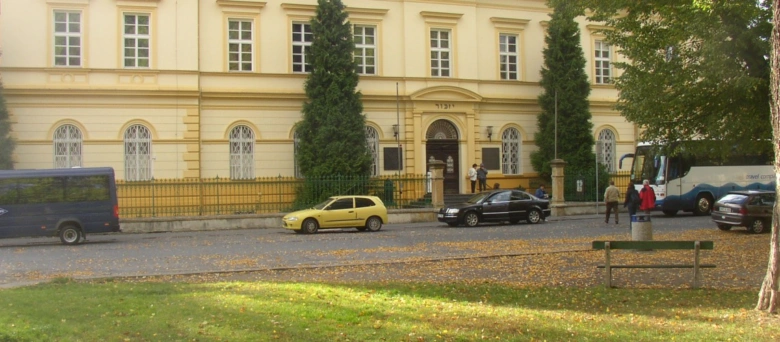 Historická budova v Terezínu s parkujícími auty před ní.