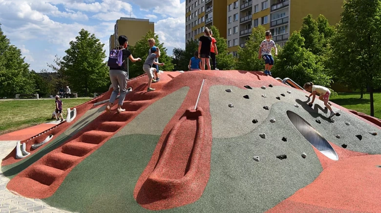 Děti hrají na barevné venkovní skluzavce s lezeckou stěnou.