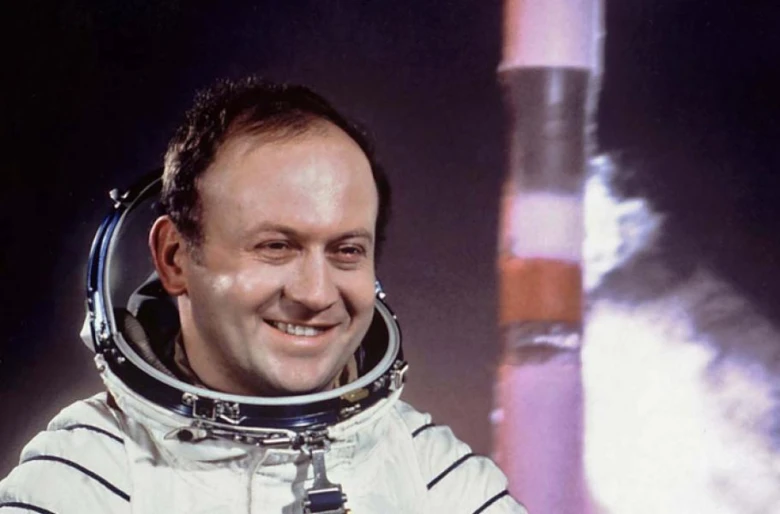Kosmonaut Vladimír Remek v obleku s raketou na pozadí.