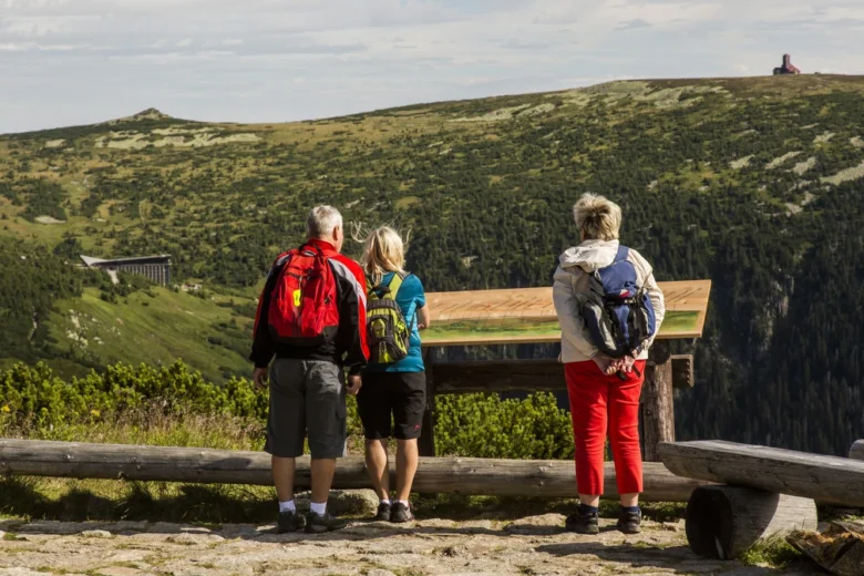Tři turisté s batohy hledí z vyhlídky na Krkonoše.