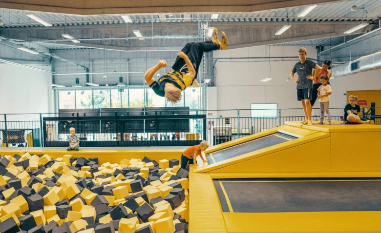 Děti skáčou na trampolín do hromady pěnových kostek.