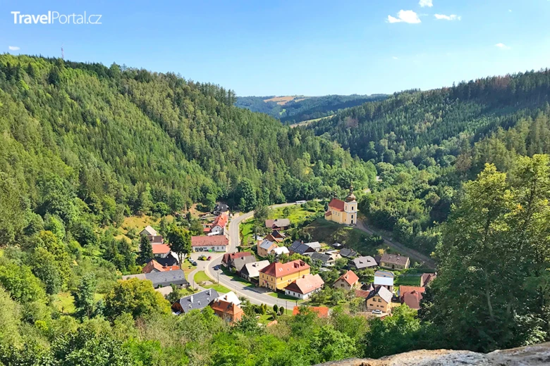Pohled na vesnici v lesním údolí pod modrou oblohou.