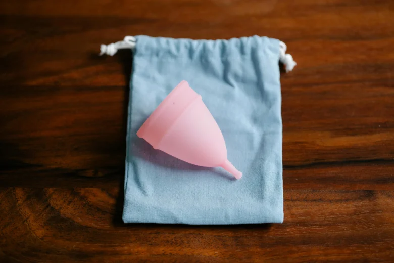 Růžový menstruační kalíšek v modrém sáčku na dřevěném stole.
