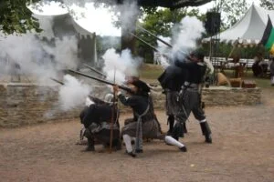 Reenactéři v kostýmech vystřelují z pušek na hradě.