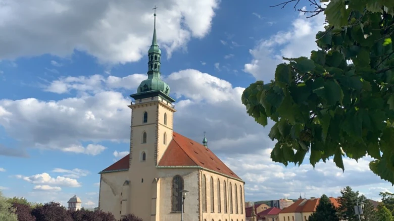 Historický kostel v Mostě s zelenou věží pod modrou oblohou.