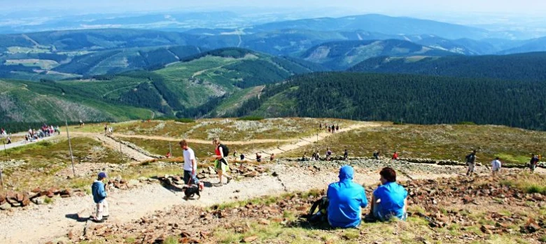 Turisté na horské stezce v Krkonoších s výhledem do krajiny.