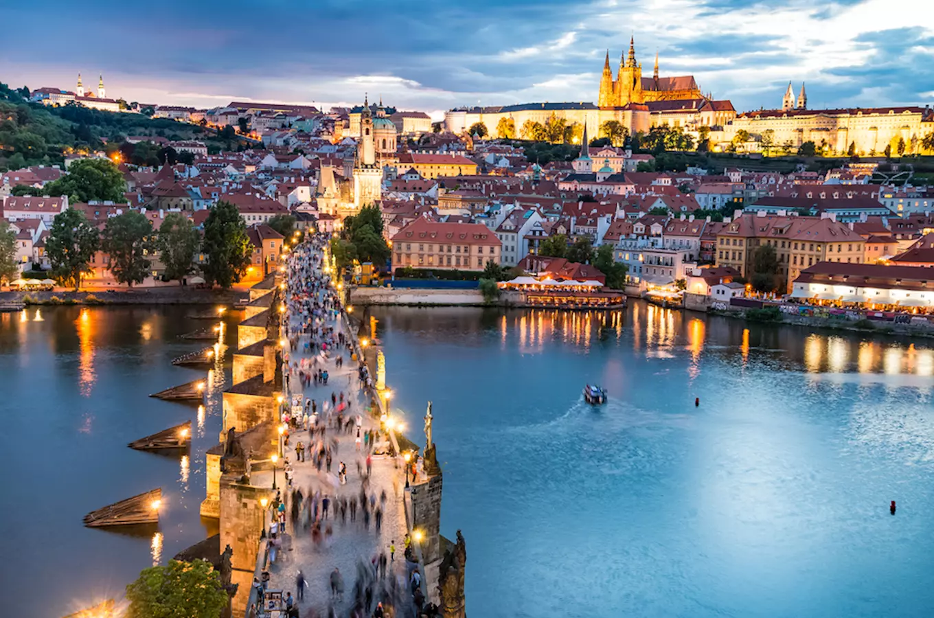 Pohled na Karlov most v Praze s lidmi při západu slunce.