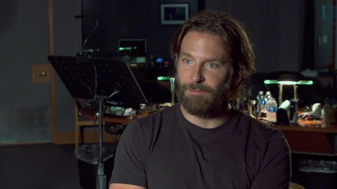 Bradley Cooper s sedí v interiéru bez úsměvu.