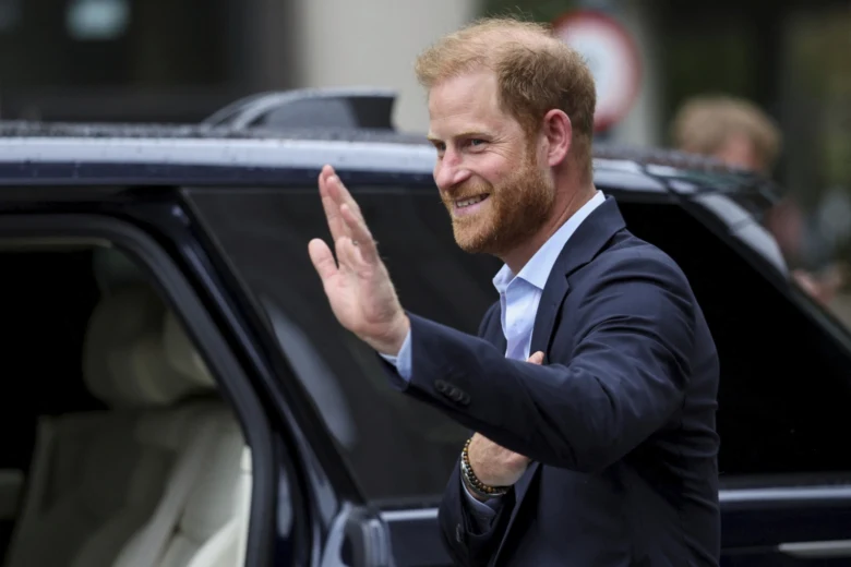 Princ Harry vyzívá z auta při veřejném vystoupení.