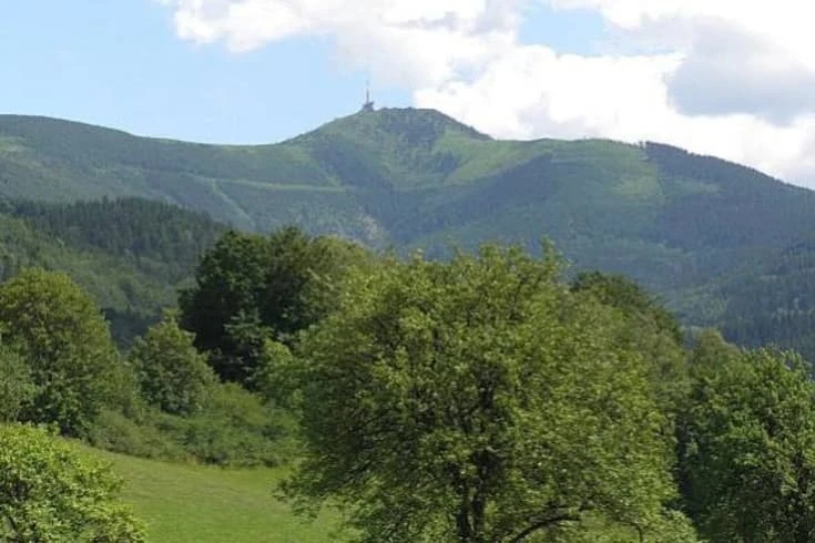 Zelené kopce Bílých Karpat s lesy a věží na vrcholu pod částečně oblohou.