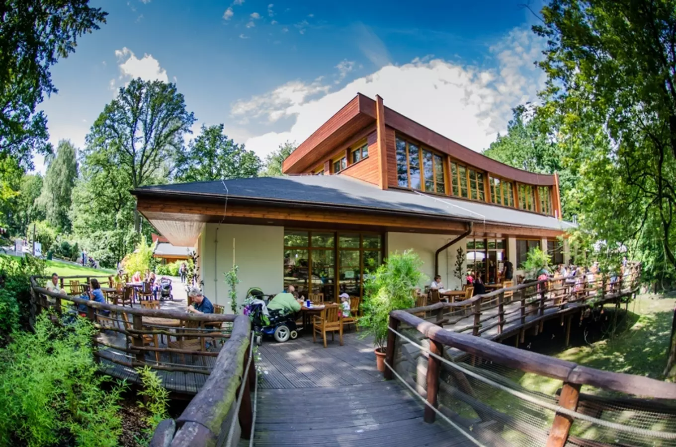 Moderní restaurace s venkovním posezením v zeleném prostředí.