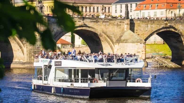 Turistická loď pluje pod mostem s cestujícími na palubě.