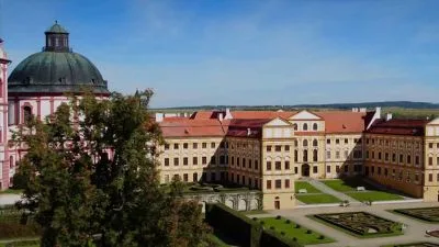 Barokní palác s zahradou a kupolí pod modrou oblohou.