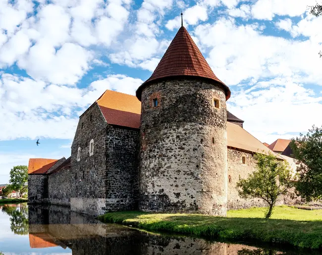 Středověký hrad s věží u řeky pod modrou oblohou.