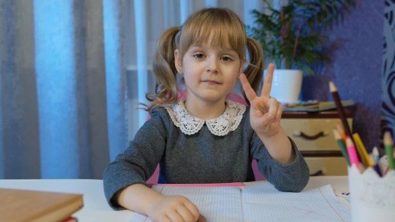 Malá dívka sedí u stolu a dělá znamení míru.