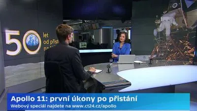 Televizní moderátor v studiu s grafikou mise Apolla 11 a astronautem na Měsíci.