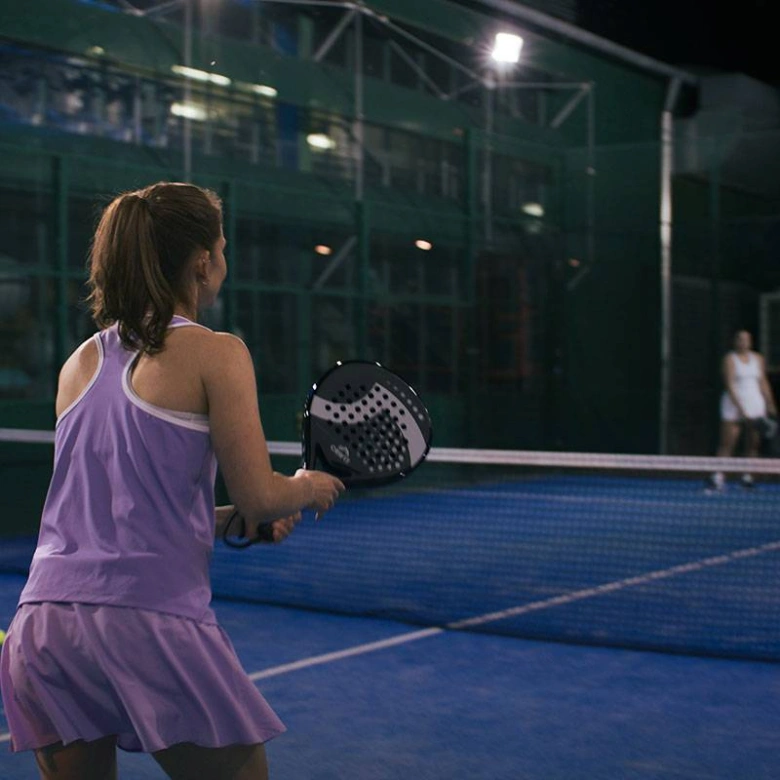 Žena v fialovém oblečení hraje padel na dvorci.