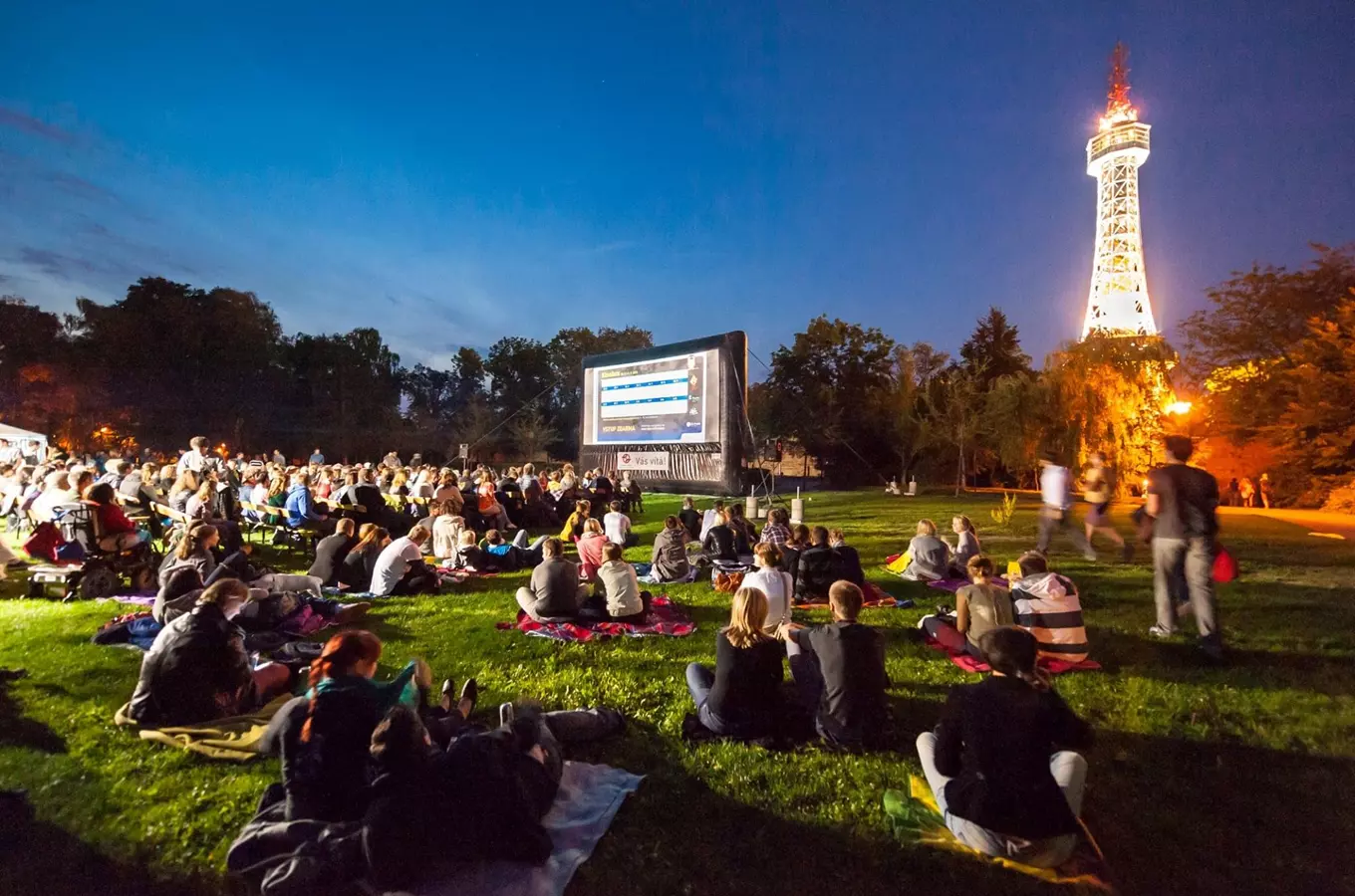 Lidé sledují film venku na letním kině v parku večer.