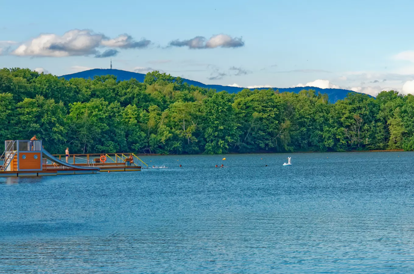 Kamencové jezero s plaveckou plošinou, lesy a horami na pozadí.