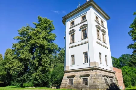 Bílá historická věž v zeleném parku pod modrou oblohou.