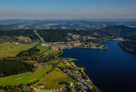 Pohled na české jezero s okolními lesy, poli a vesnicemi.