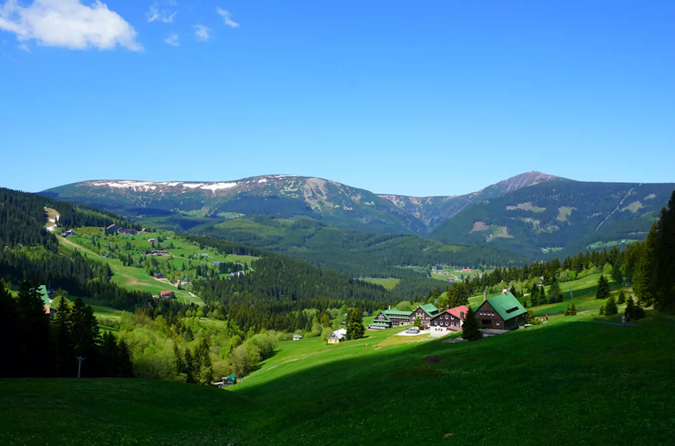 Pohled na vesnici v horách s domy a lesy pod Sněžkou.