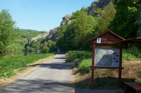 Zelená stezka vedoucí kolem skalnatého útesu s informační tabulí.