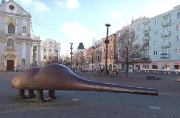 Bronzová socha dinosaura na náměstí v Opavě s historickými budovami.
