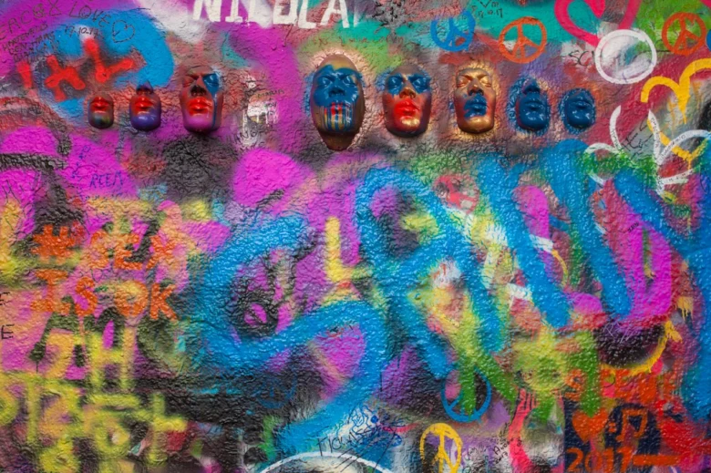 Lennonova zeď v Praze s barevnou grafití a sochami tváří.