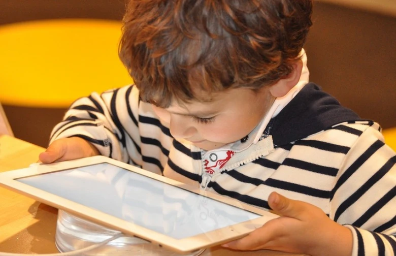 Malý chlapec se soustředěně dívá na bílý tablet.