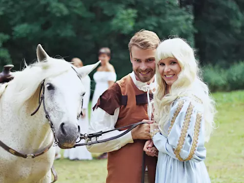 Muž a žena v kostýmech stojí vedle bílého koně na trávníku.