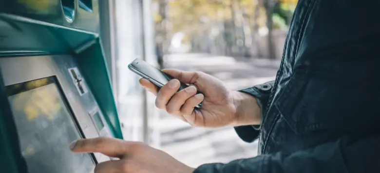 Osoba vkládá hotovost do bankomatu pomocí chytrého telefonu.