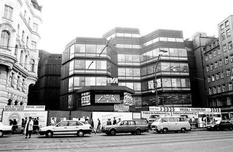 Černobílá fotografie brutalistické budovy v pražské ulici s auty.