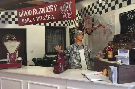 Interiér starobuďího řeznictví s figurínou a visícími uzenými masy.