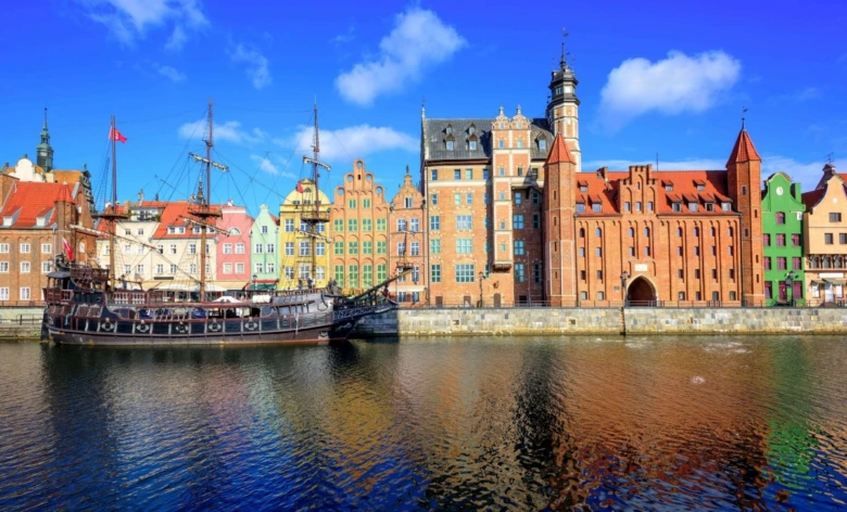 Historické budovy v Gdansk na břehu řeky pod modrou oblohou.