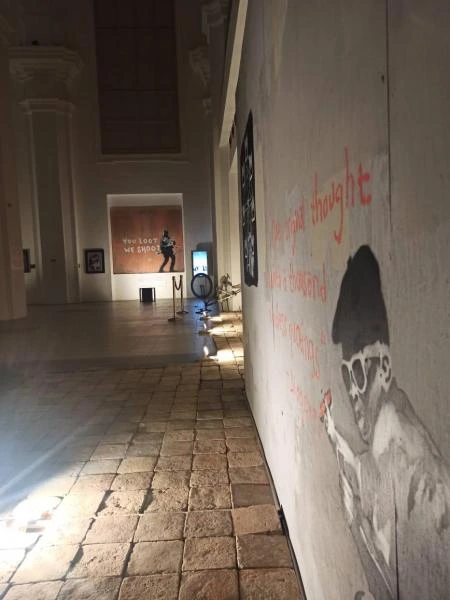 Banksyho umění v galerii s grafitovou postavou na zdi.